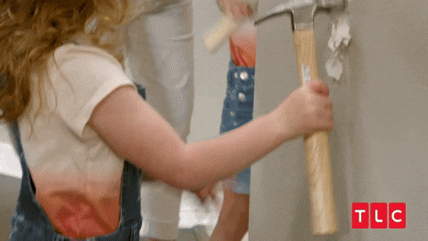 Una bambina impugna con entusiasmo una mazza da demolizione e sfascia un muro di cartongesso durante una puntata di una trasmissione di TLC